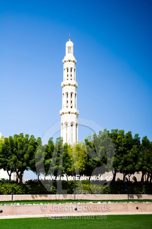 An ornate stone minaret towers over lush gardens in the Grand Mosque. Sultan Qaboos Grand Mosque, Muscat, Sultanate of Oman.