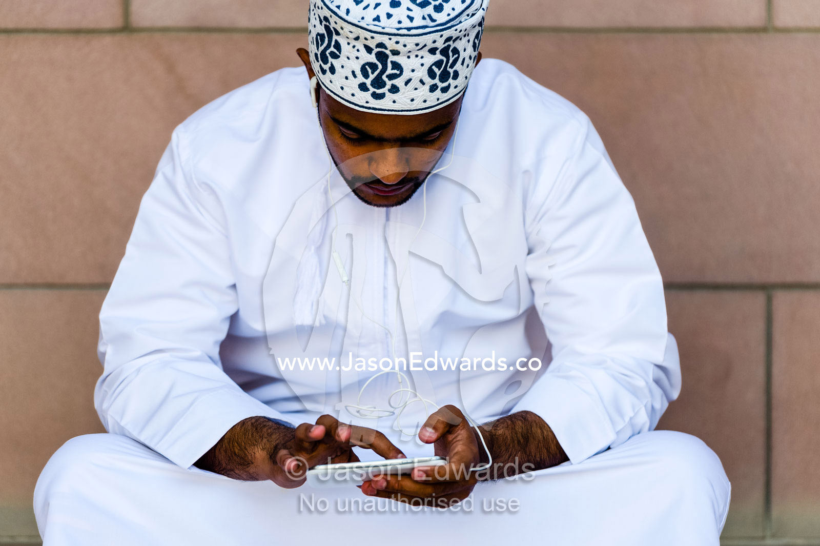 A Muslim man in a dishdasha and kuma texting on his mobile phone at the Grand Mosque. Sultan Qaboos Grand Mosque, Muscat, Sultanate of Oman.