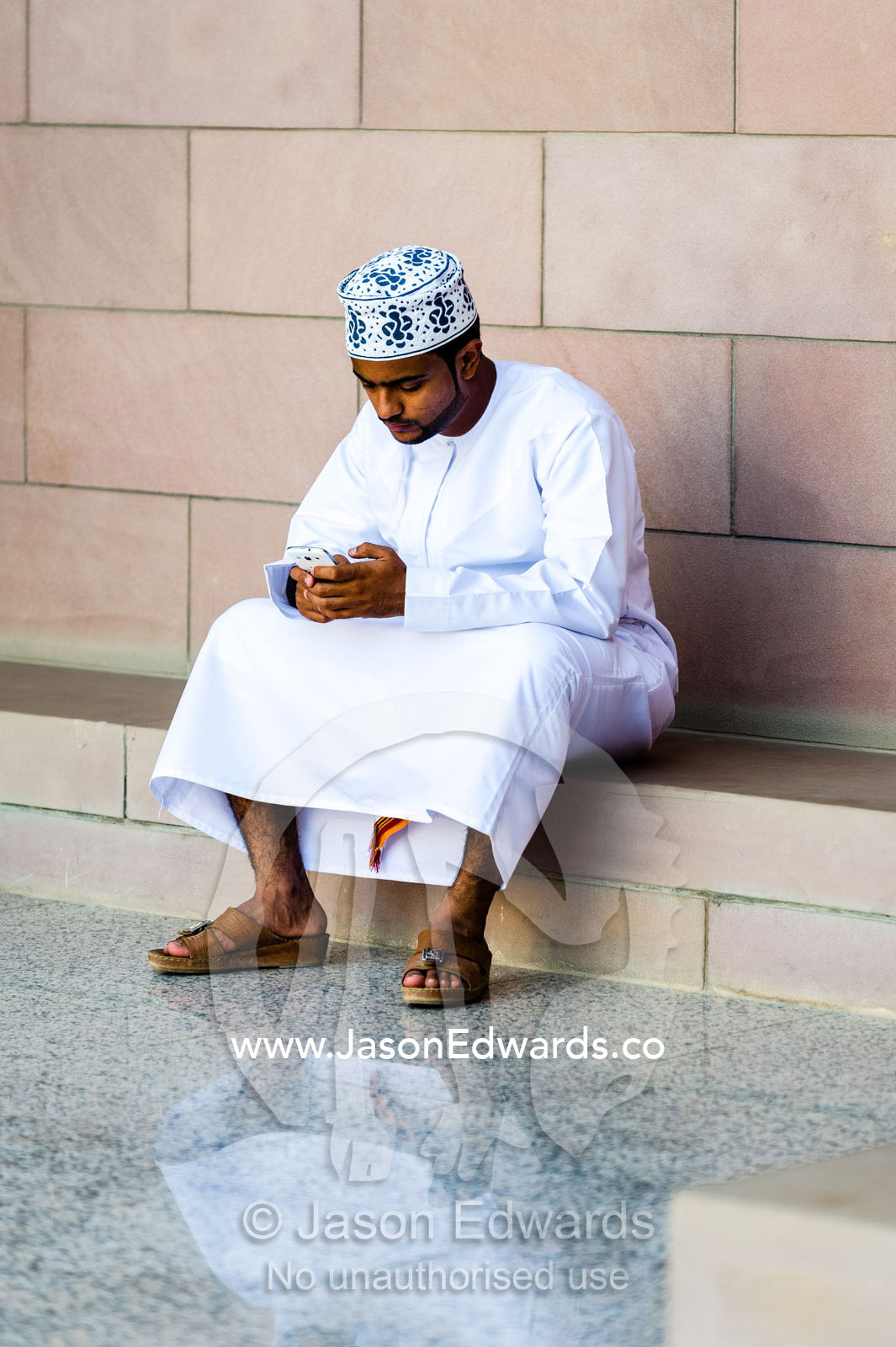 A Muslim man in a dishdasha and kuma texting on his mobile phone at the Grand Mosque. Sultan Qaboos Grand Mosque, Muscat, Sultanate of Oman.