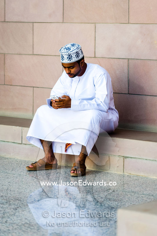 A Muslim man in a dishdasha and kuma texting on his mobile phone at the Grand Mosque. Sultan Qaboos Grand Mosque, Muscat, Sultanate of Oman.