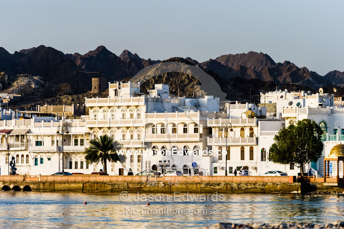 Desert mountains tower over whitewashed walls of a shopping and hotel district on the shores of the Gulf of Oman. Muscat, Gulf of Oman, Sultanate of Oman.