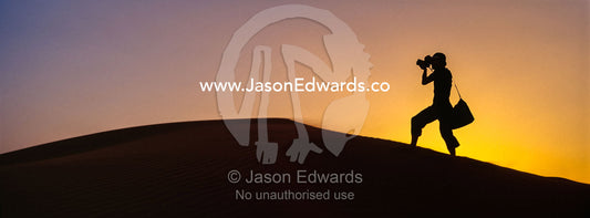 The silhouette of a photographer taking photos on a sand dune at sunset. Wahiba Sands, Ramlat al-Wahiba, Sharqiya Sands, Sultanate of Oman.