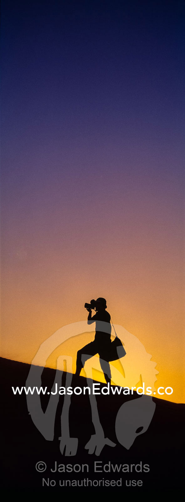 The silhouette of a photographer taking photos on a sand dune at sunset. Wahiba Sands, Ramlat al-Wahiba, Sharqiya Sands, Sultanate of Oman.