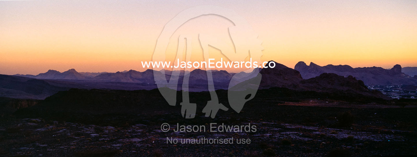 Pastel sunset afterglow on the horizon above jagged deserts mountains. Al Hajar Mountains, Al Hamra, Ad Dakhiliyah Region, Sultanate of Oman.