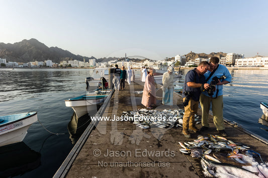A photographer instructing a scholarship recipient about photography at a fish market. Mutrah Fish Market, Muscat, Gulf of Oman, Sultanate of Oman.