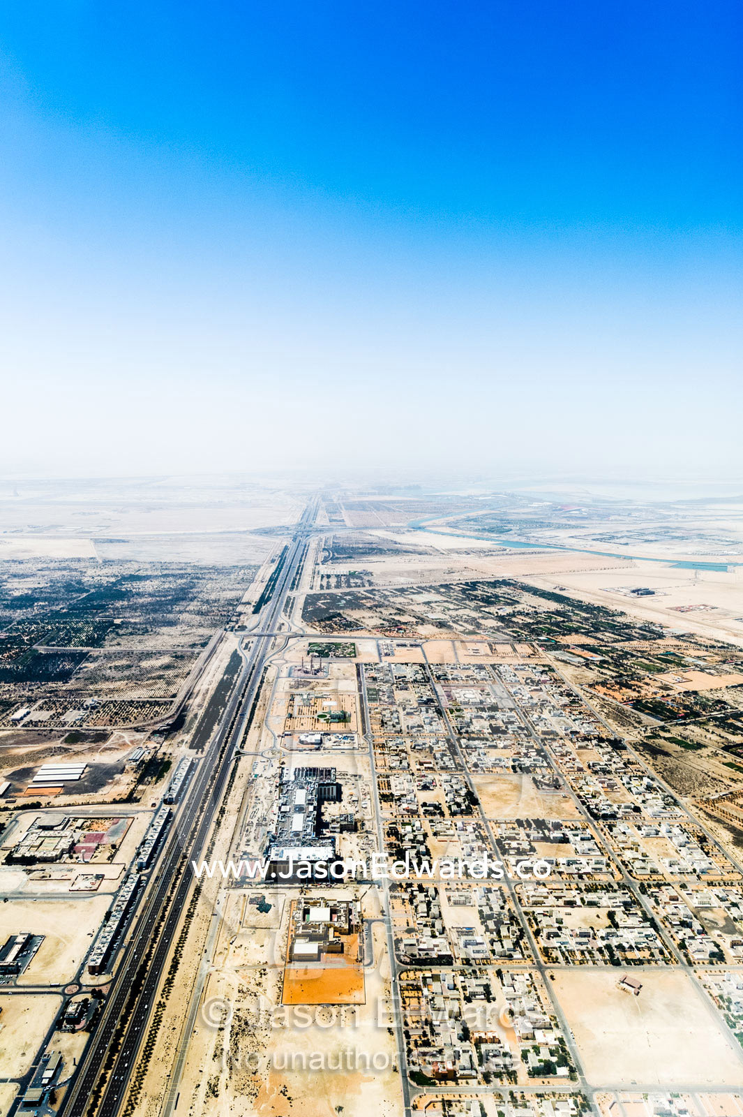 A long straight highway crosses the desert past suburban residential estates. Emirate of Abu Dhabi, Abu Dhabi, Persian Gulf, United Arab Emirates.