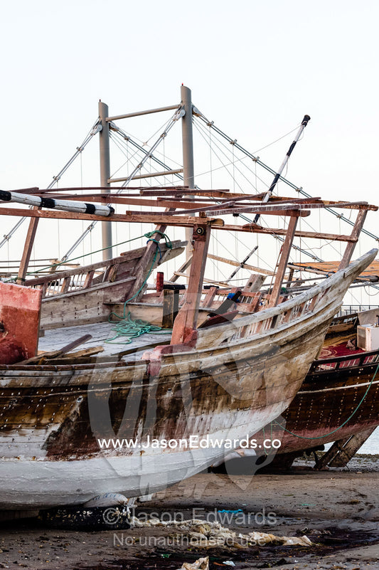 A dhow rests on the mud on a beach at low tide. Sur, Ash Sharqiyah Region, Gulf of Oman, Sultanate of Oman.