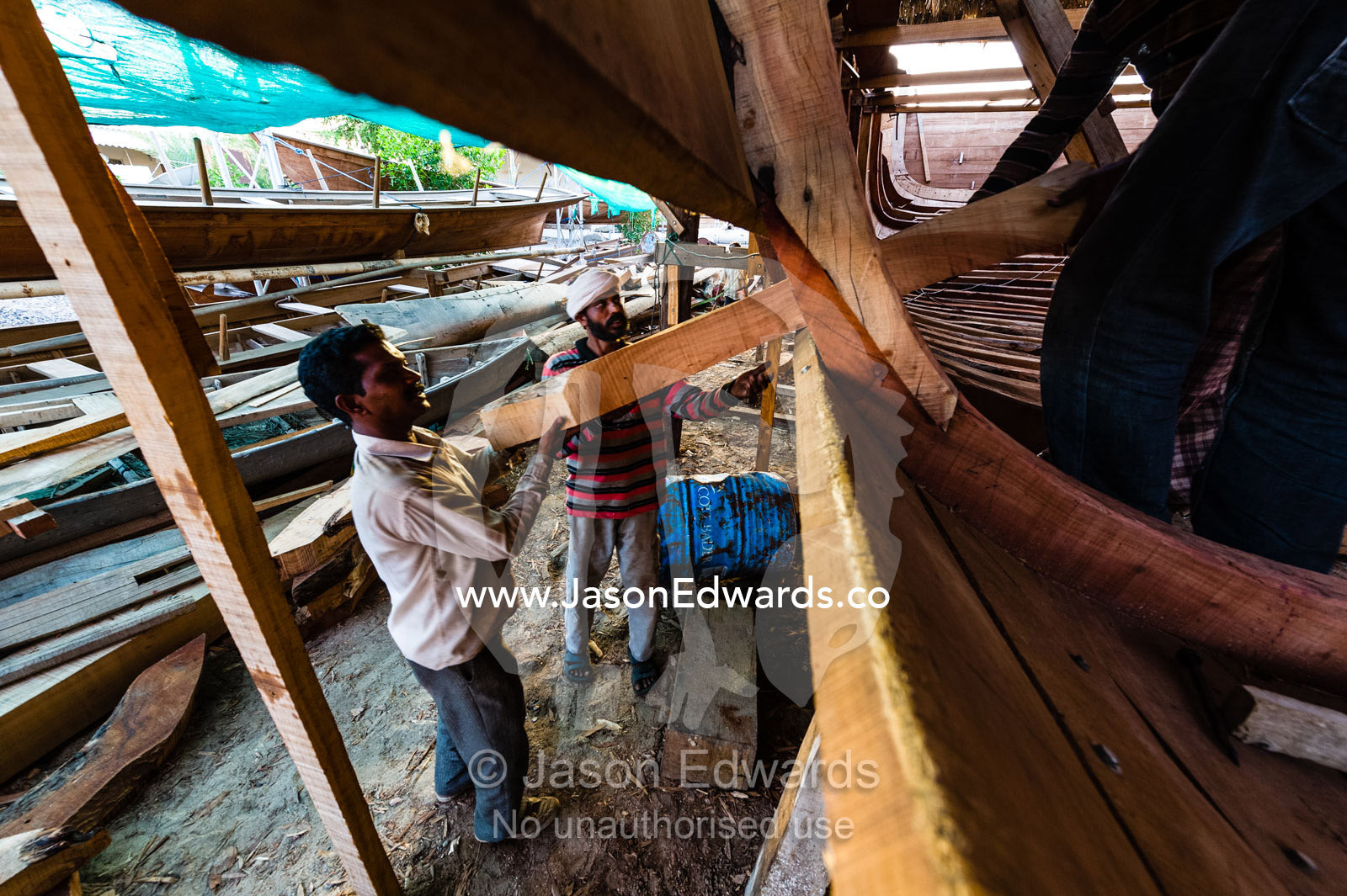 Laborers carry timber hull ribs during the handmade construction of an ancient timber dhow. Sur, Ash Sharqiyah Region, Gulf of Oman, Sultanate of Oman.