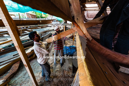Laborers carry timber hull ribs during the handmade construction of an ancient timber dhow. Sur, Ash Sharqiyah Region, Gulf of Oman, Sultanate of Oman.
