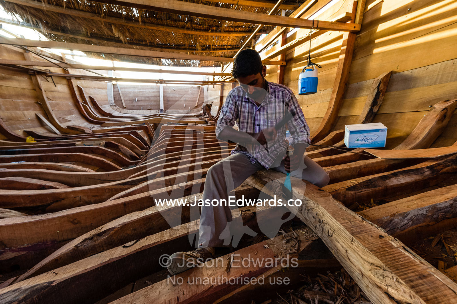 Laborers chisel and shape timber hull ribs during handmade construction of an ancient timber dhow. Sur, Ash Sharqiyah Region, Gulf of Oman, Sultanate of Oman.