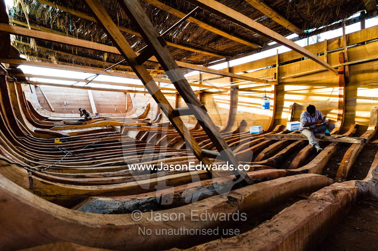 A ladder descends from the deck to the timber ribs of a wooden dhow during construction. Sur, Ash Sharqiyah Region, Gulf of Oman, Sultanate of Oman.