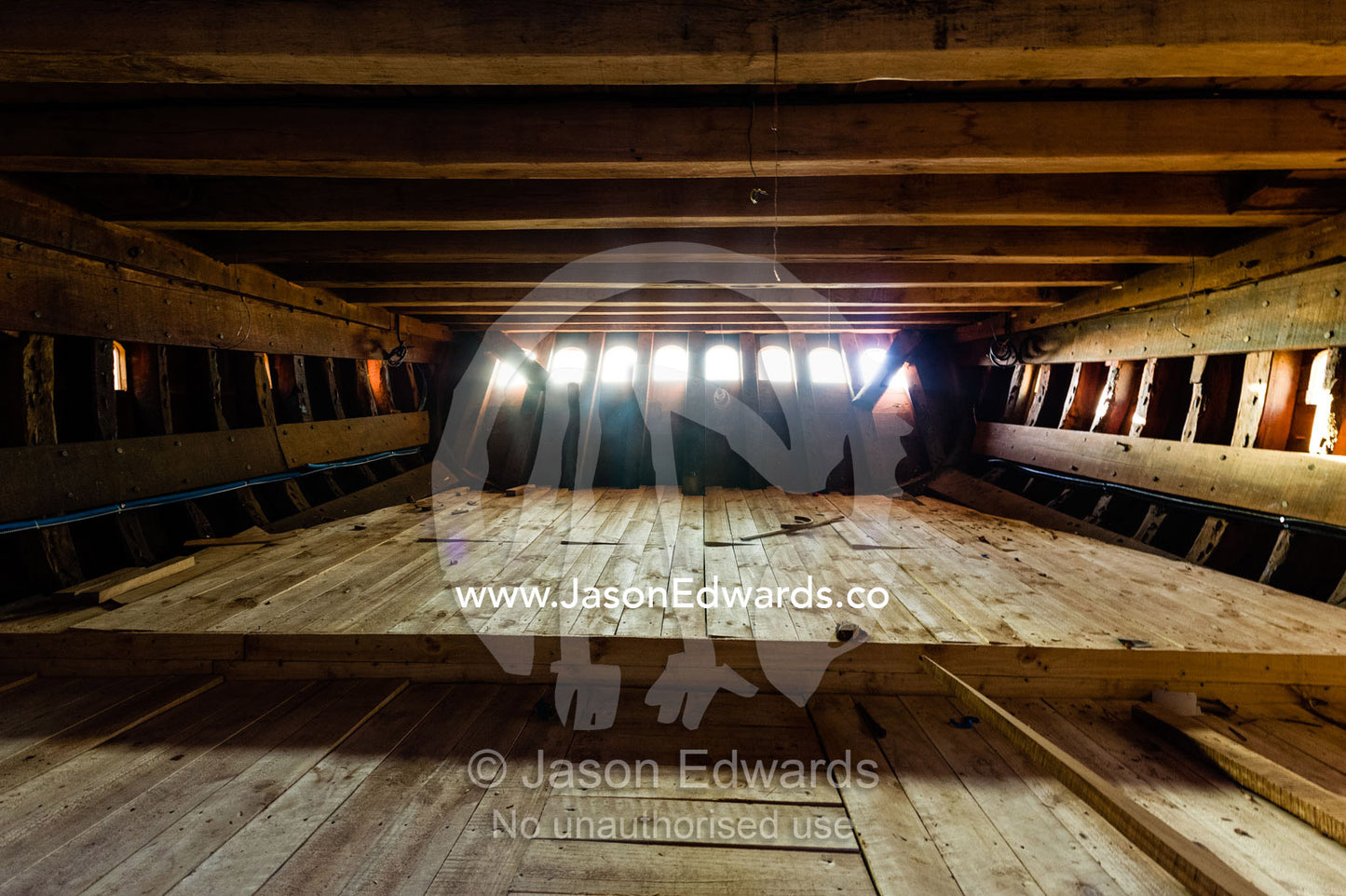 Sunlight illuminates raw timber deck planks inside a dhow during construction. Sur, Ash Sharqiyah Region, Gulf of Oman, Sultanate of Oman.