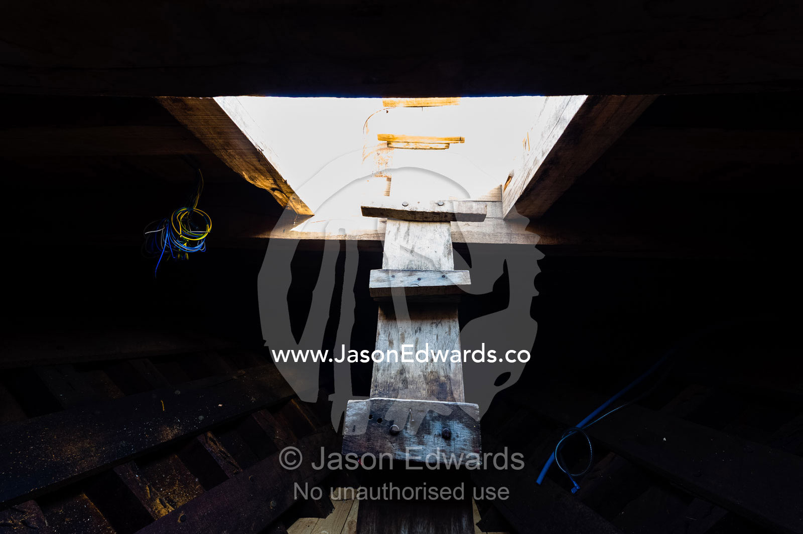 A timber ladder descends into the darkness of a dhow hull during construction. Sur, Ash Sharqiyah Region, Gulf of Oman, Sultanate of Oman.