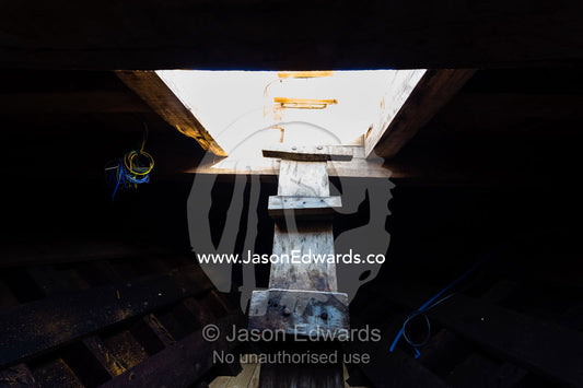 A timber ladder descends into the darkness of a dhow hull during construction. Sur, Ash Sharqiyah Region, Gulf of Oman, Sultanate of Oman.