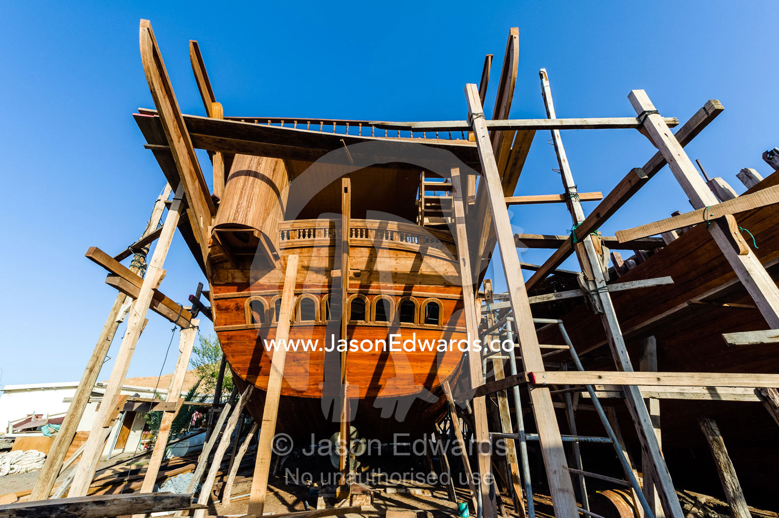 Scaffolding supports the hull during handmade construction of an ancient timber dhow in a ship building yard. Sur, Ash Sharqiyah Region, Gulf of Oman, Sultanate of Oman.