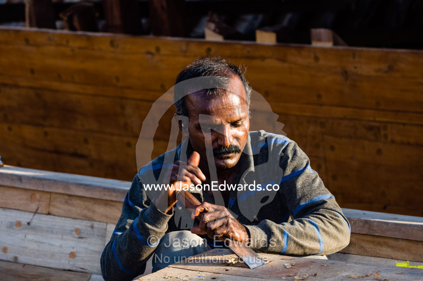 A laborer shapes timber with a hammer and chisel in a dhow ship building yard. Sur, Ash Sharqiyah Region, Gulf of Oman, Sultanate of Oman.