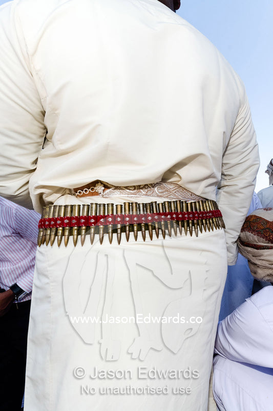 A bandolier of bullets decorates the waist belt of a di dash at a camel race event. Bidiya, Sharqiya Region, Sultanate of Oman.