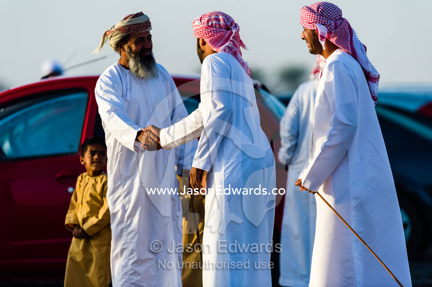 Muslim men wearing dishdasha and masar shake hands as they greet each other to watch camel races. Bidiya, Sharqiya Region, Sultanate of Oman.