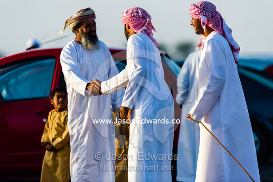 Muslim men wearing dishdasha and masar shake hands as they greet each other to watch camel races. Bidiya, Sharqiya Region, Sultanate of Oman.