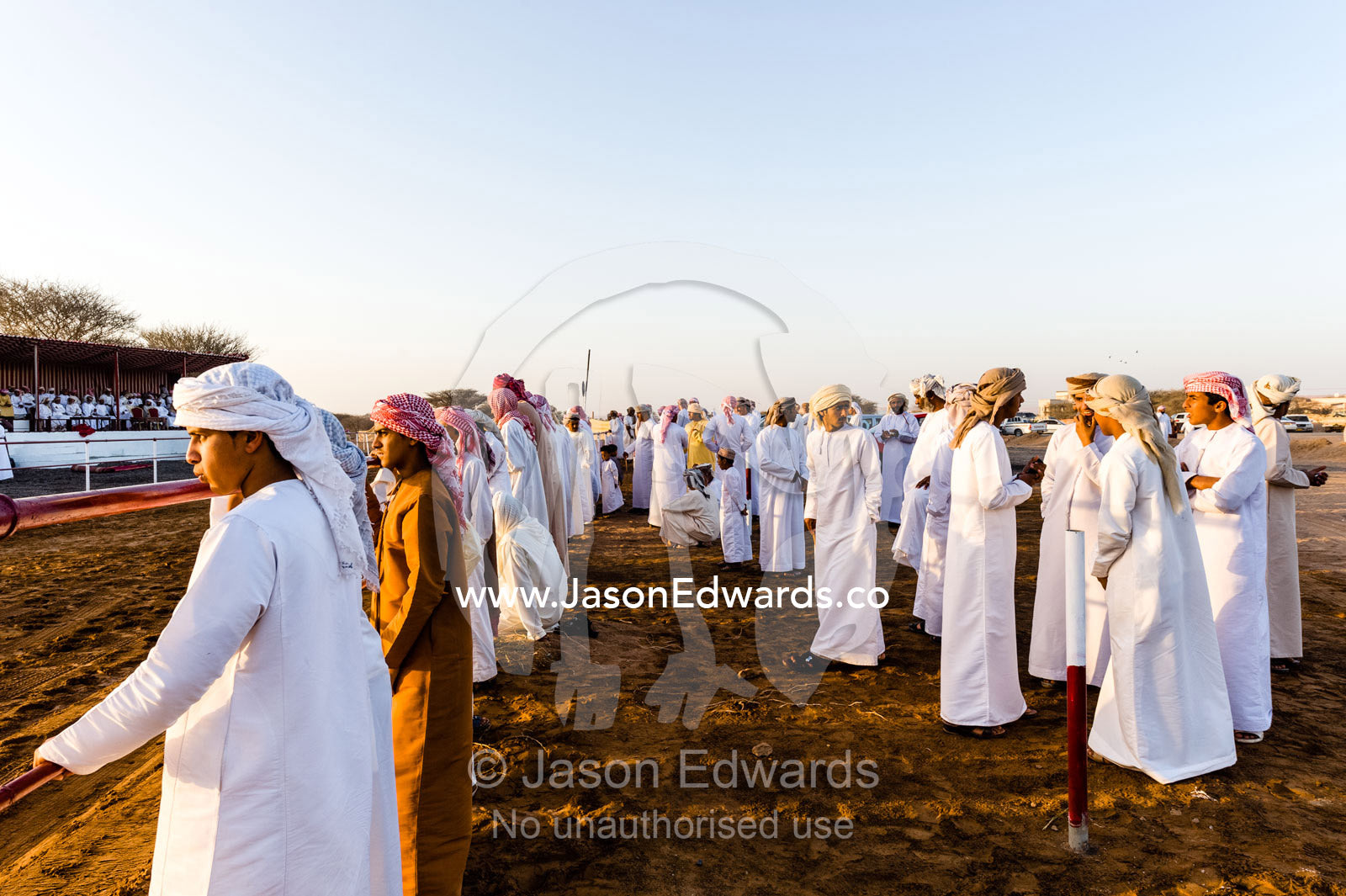 A crowd of Muslim men and boys wearing dishdasha and masar gather to watch camel races. Bidiya, Sharqiya Region, Sultanate of Oman.
