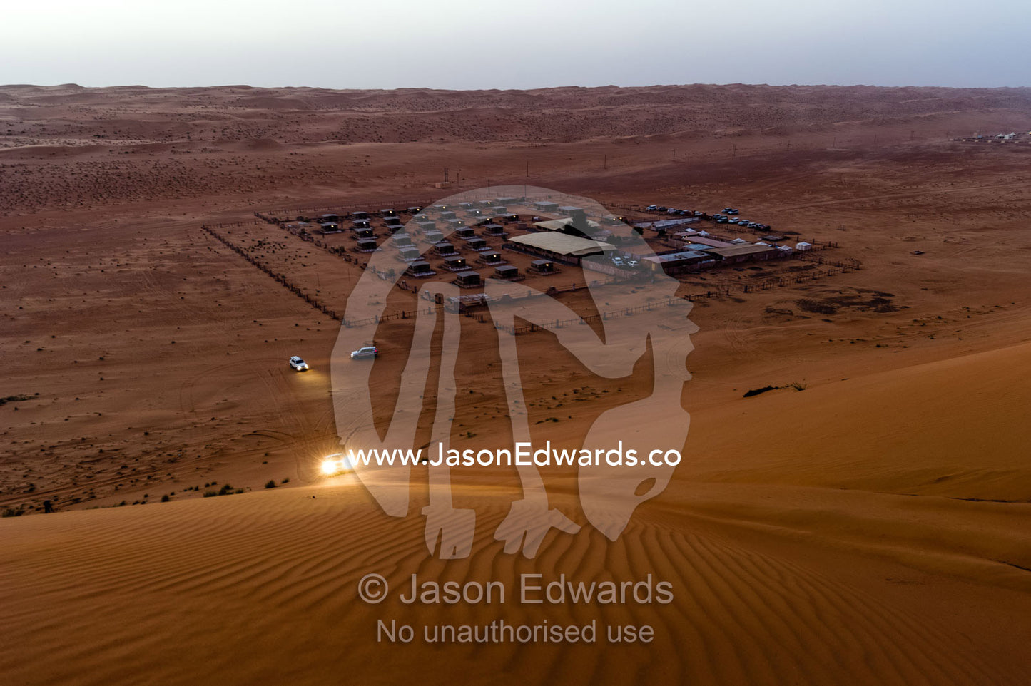 A 4WD ascends a sand dune at night above a desert camp. Wahiba Sands, Ramlat al-Wahiba, Sharqiya Sands, Sultanate of Oman.