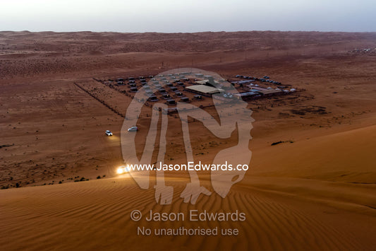 A 4WD ascends a sand dune at night above a desert camp. Wahiba Sands, Ramlat al-Wahiba, Sharqiya Sands, Sultanate of Oman.