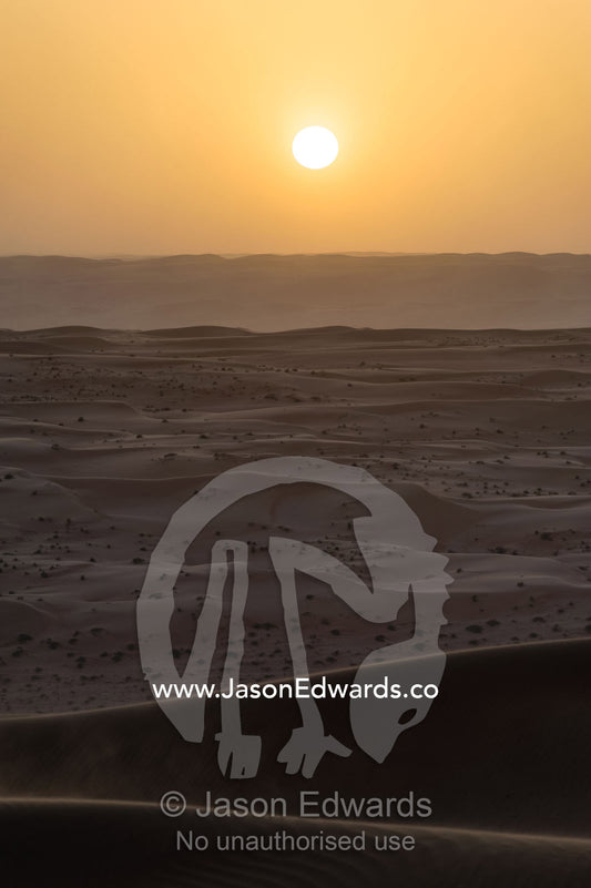 Windblown sand dunes fold across the desert towards the distant horizon at sunset. Wahiba Sands, Ramlat al-Wahiba, Sharqiya Sands, Sultanate of Oman.