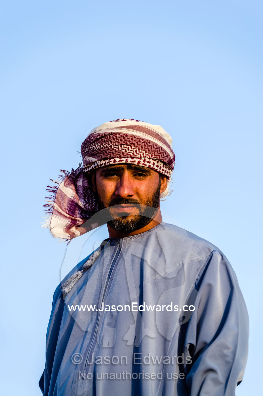 A Muslim man standing on a sand dune at sunset wearing a traditional dishdasha and masar. Wahiba Sands, Ramlat al-Wahiba, Sharqiya Sands, Sultanate of Oman.