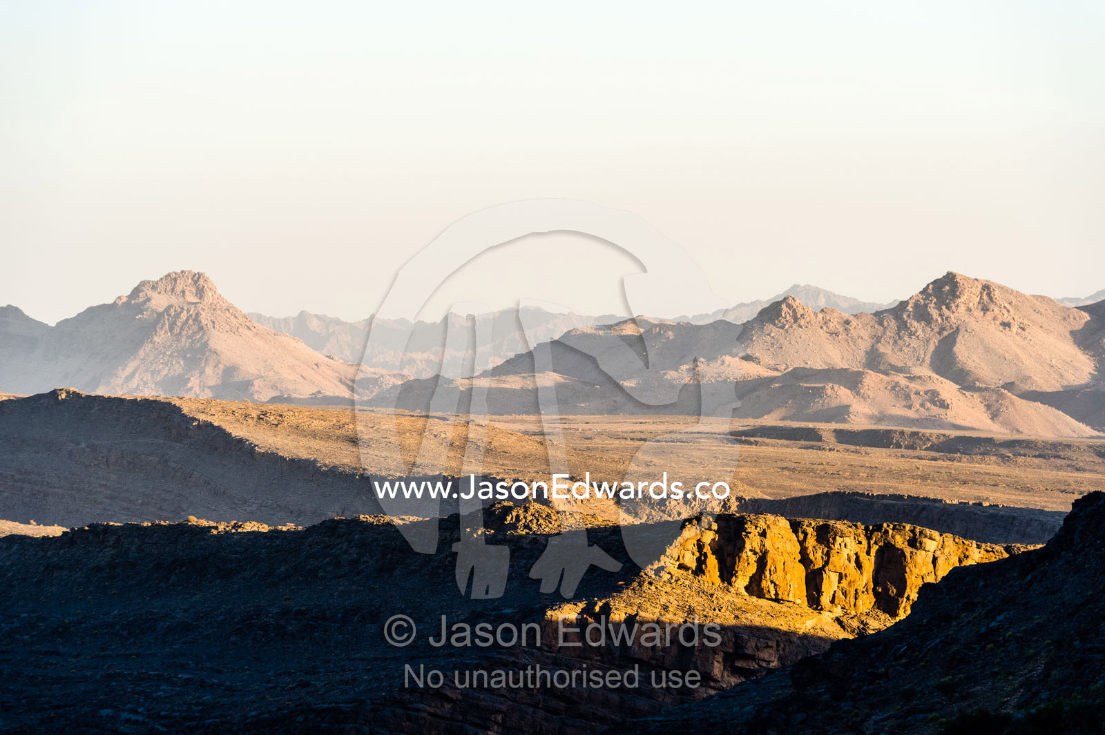 Sunset catches jagged mountain peaks and valleys in a desert. Al Hajar Mountains, Al Hamra, Ad Dakhiliyah Region, Sultanate of Oman.