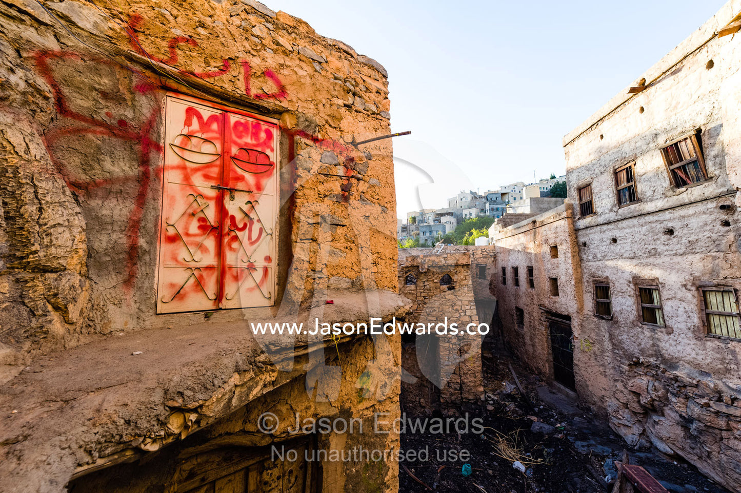 Red graffiti paint on a steel door and wall in an ancient mud brick village. Misfat Al Abryeen, Al Hajar Mountains, Al Hamra, Ad Dakhiliyah Region, Sultanate of Oman.