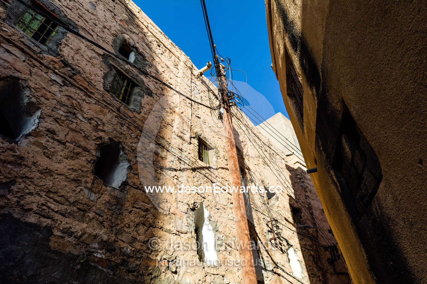 Electrical cables and electricity pole in a narrow mud brick alleyway in an ancient village. Misfat Al Abryeen, Al Hajar Mountains, Al Hamra, Ad Dakhiliyah Region, Sultanate of Oman.
