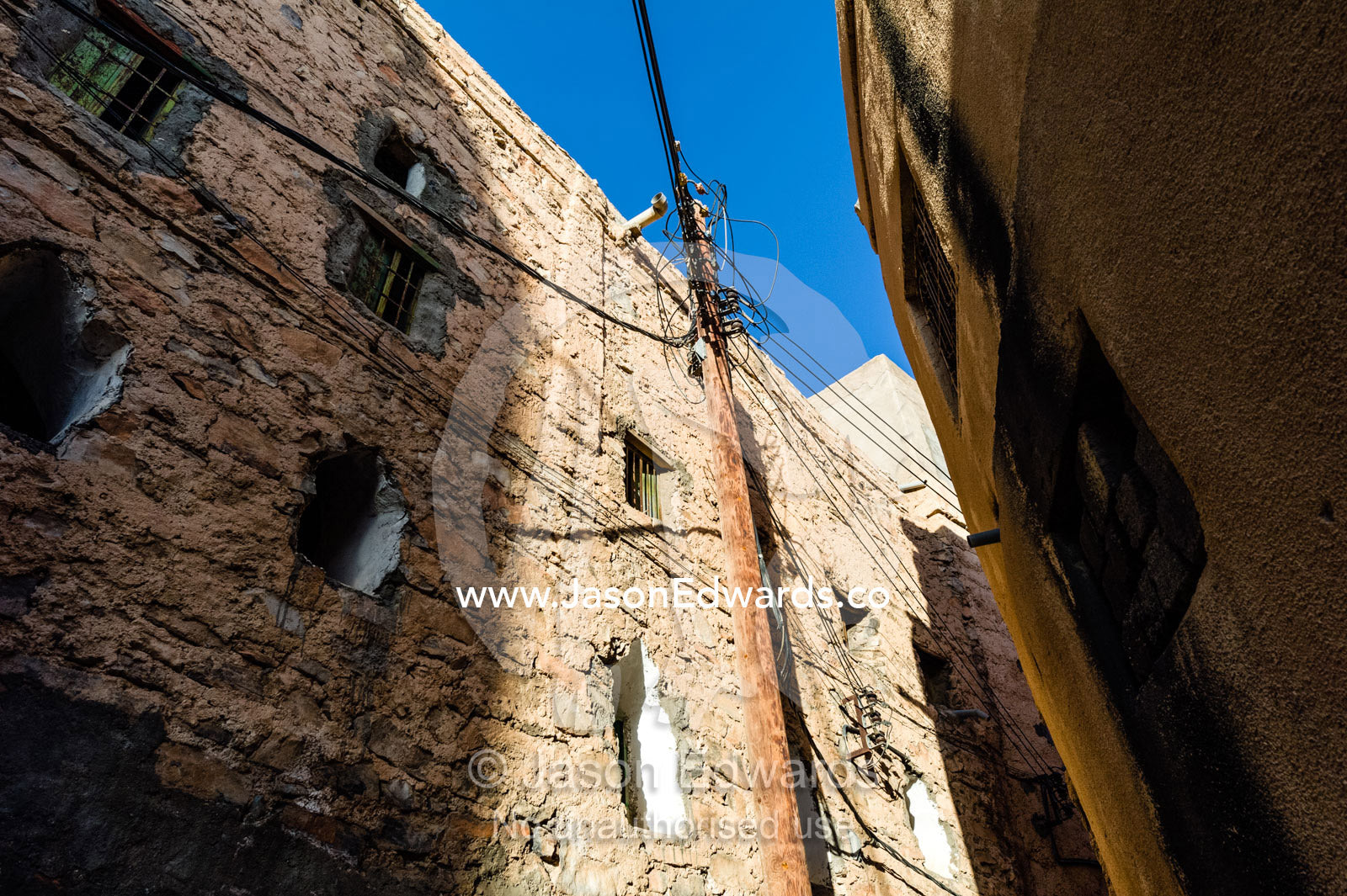 Electrical cables and electricity pole in a narrow mud brick alleyway in an ancient village. Misfat Al Abryeen, Al Hajar Mountains, Al Hamra, Ad Dakhiliyah Region, Sultanate of Oman.