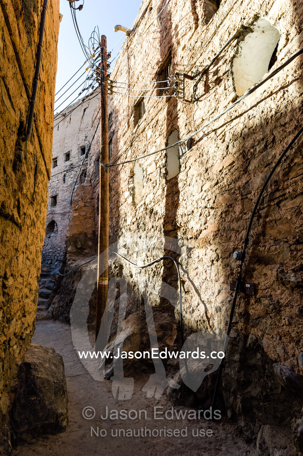 Electrical cables and electricity pole in a narrow mud brick alleyway in an ancient village. Misfat Al Abryeen, Al Hajar Mountains, Al Hamra, Ad Dakhiliyah Region, Sultanate of Oman.