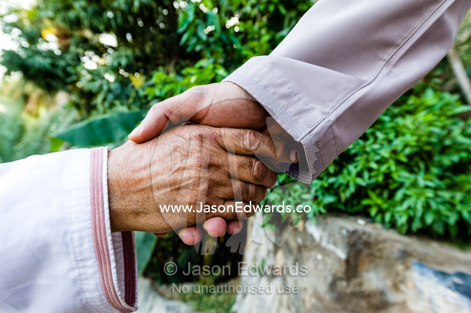 A pair of Muslim men wearing traditional dishdasha shake hands in greeting. Misfat Al Abryeen, Al Hajar Mountains, Al Hamra, Ad Dakhiliyah Region, Sultanate of Oman.