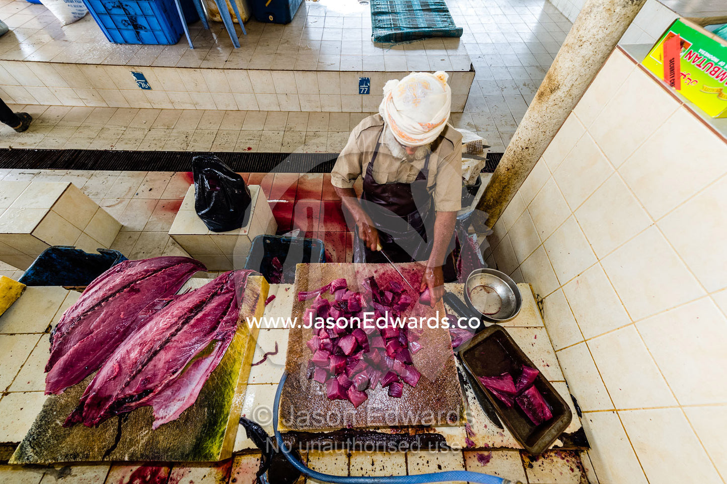 A vendor cuts the pink flesh of a tuna into cubes for sale in a fish market. Mutrah Fish Market, Muscat, Gulf of Oman, Sultanate of Oman.