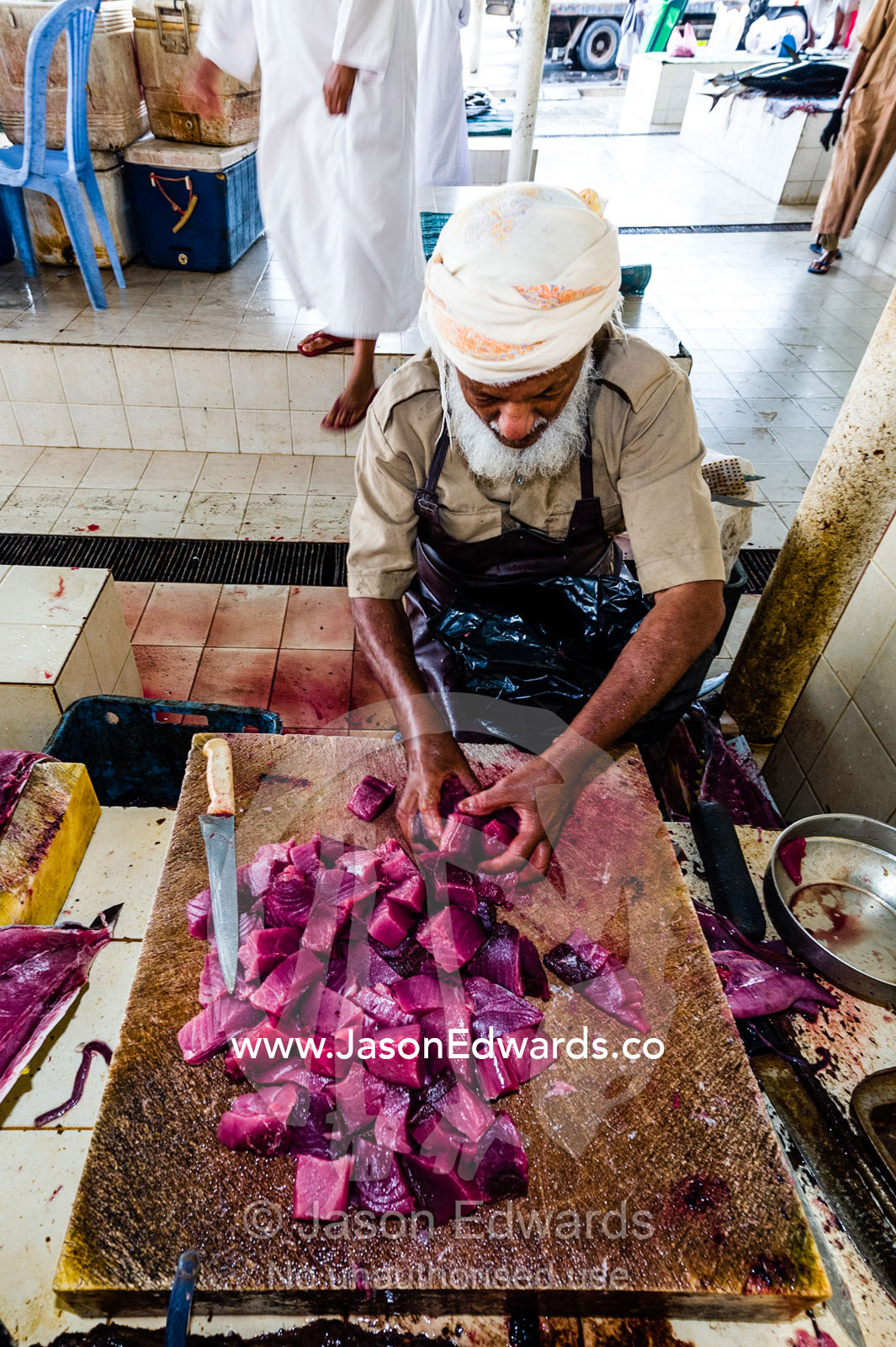 A vendor cuts the pink flesh of a tuna into cubes for sale in a fish market. Mutrah Fish Market, Muscat, Gulf of Oman, Sultanate of Oman.