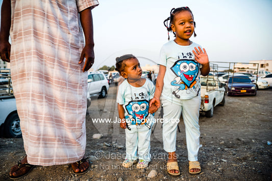 Young sisters watch a traditional bull fight with their father. Al Sharadi, Seeb, Muscat, Sultanate of Oman.