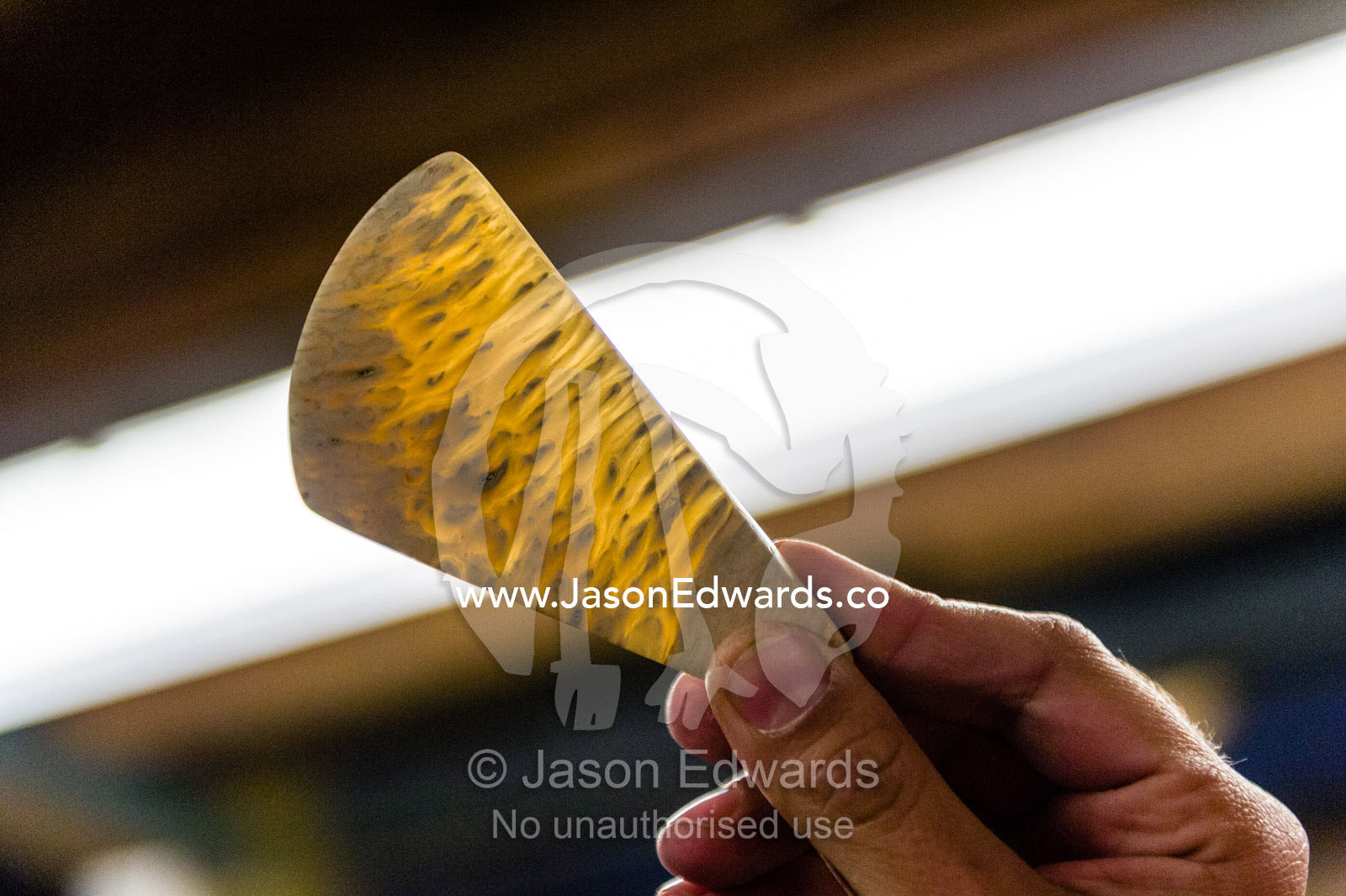 An artist holds a piece of jewellery against a light to show it's translucent structure. Kangerlussuaq, Qeqqata Municipality, Greenland.