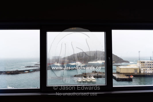 Looking through insulated windows on a rainy afternoon over a fishing port. Maniitsoq, Sukkertoppen, Qeqqata Municipality, Greenland.