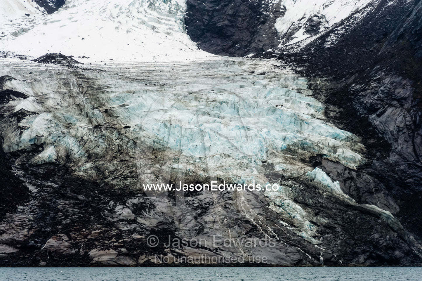 A jagged glacier tongue recedes up and rugged and inhospitable mountain gorge in a fiord. Fjord of Eternity, Maniitsoq, Sukkertoppen, Qeqqata Municipality, Greenland.