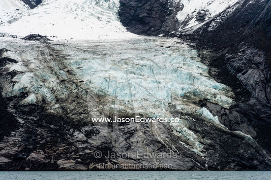 A jagged glacier tongue recedes up and rugged and inhospitable mountain gorge in a fiord. Fjord of Eternity, Maniitsoq, Sukkertoppen, Qeqqata Municipality, Greenland.
