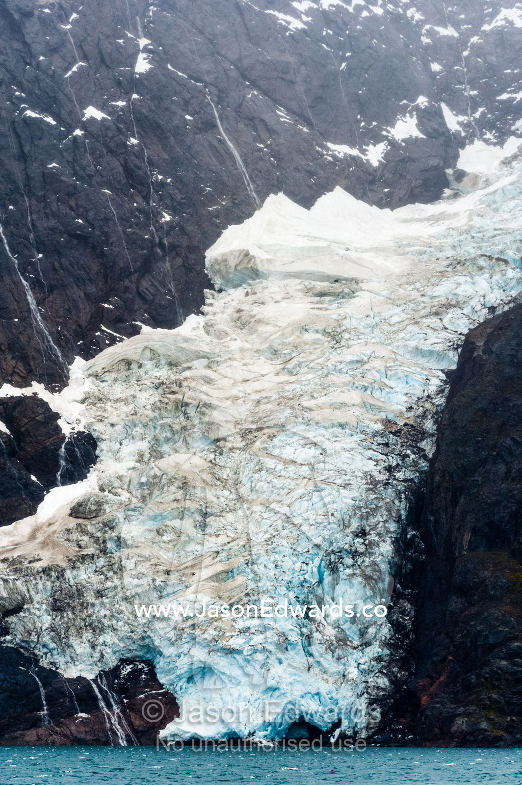 A jagged glacier tongue recedes up and rugged and inhospitable mountain gorge in a fiord. Fjord of Eternity, Maniitsoq, Sukkertoppen, Qeqqata Municipality, Greenland.