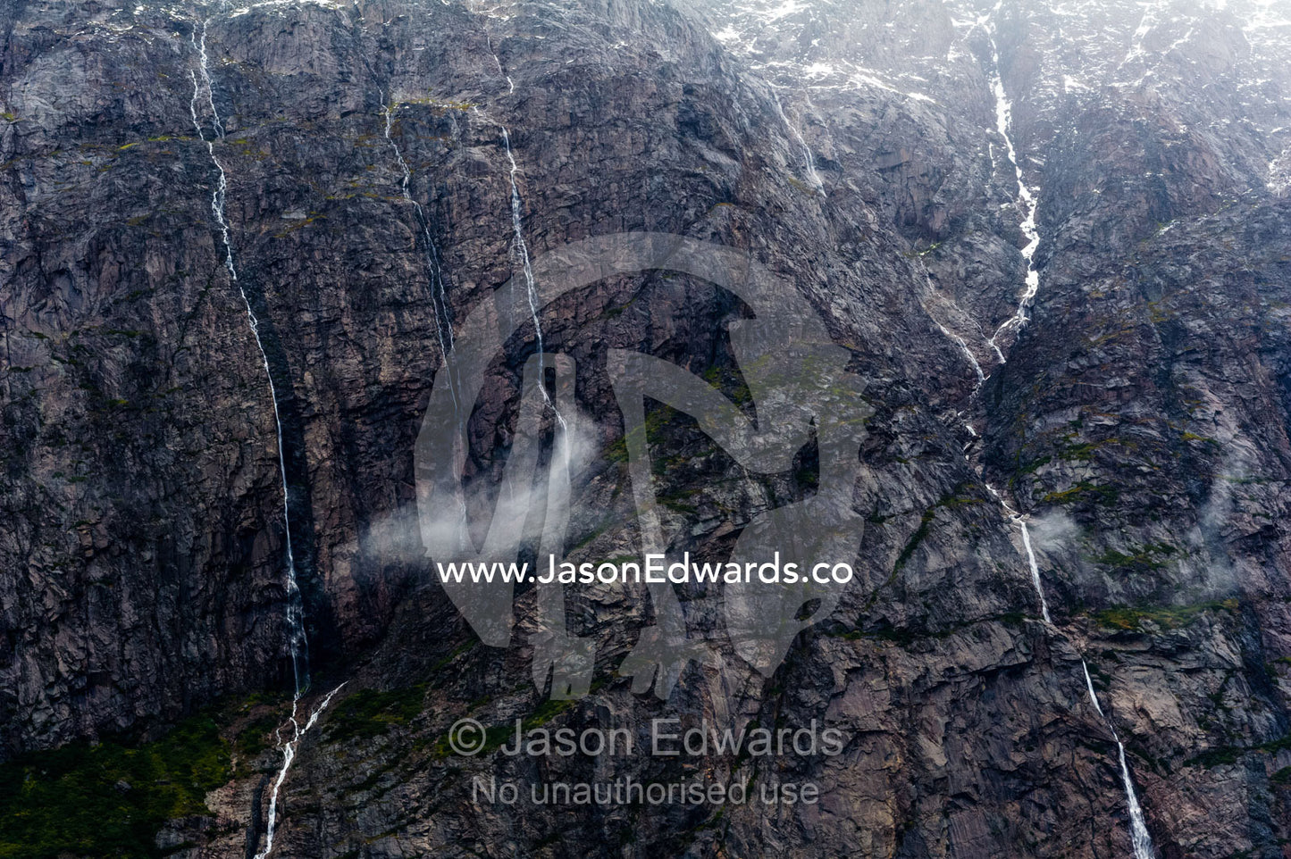 Waterfalls cascade down sheer cliffs into the ocean from melting glaciers in a fiord. Fjord of Eternity, Maniitsoq, Sukkertoppen, Qeqqata Municipality, Greenland.