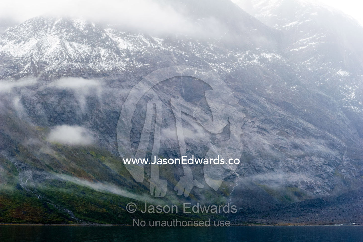 Cloud and mist shroud jagged and rugged mountain peaks during a rain storm in a fiord. Fjord of Eternity, Maniitsoq, Sukkertoppen, Qeqqata Municipality, Greenland.