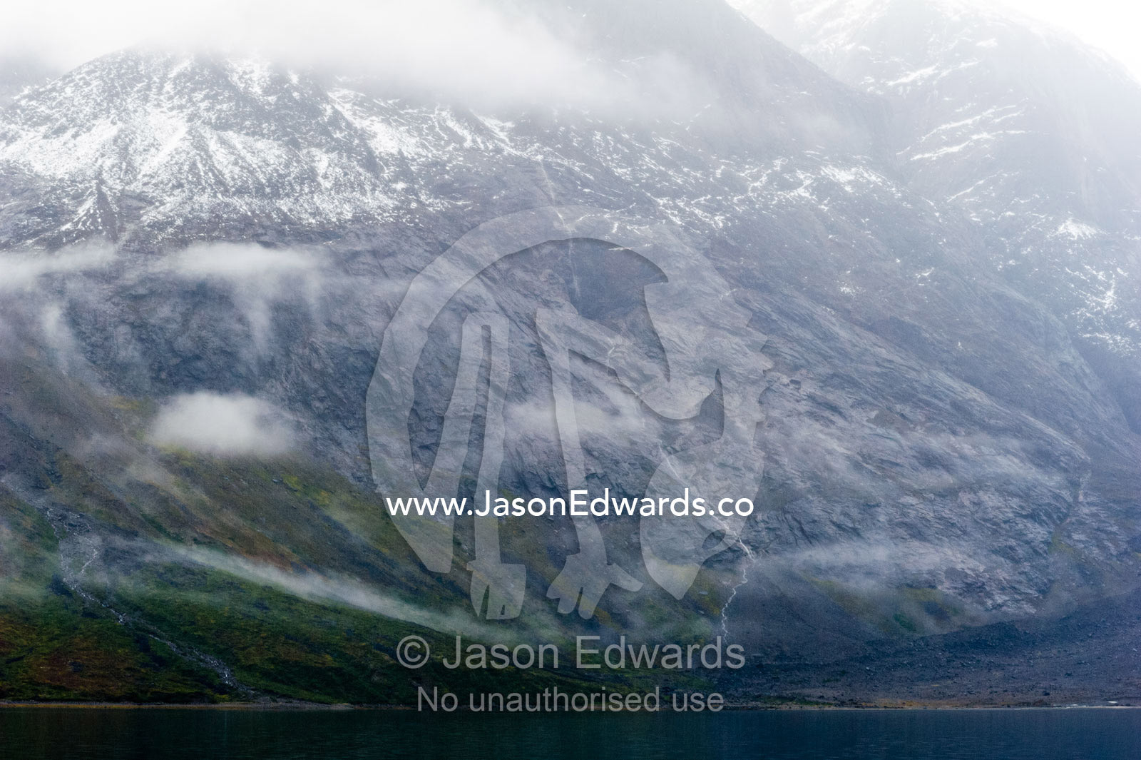 Cloud and mist shroud jagged and rugged mountain peaks during a rain storm in a fiord. Fjord of Eternity, Maniitsoq, Sukkertoppen, Qeqqata Municipality, Greenland.
