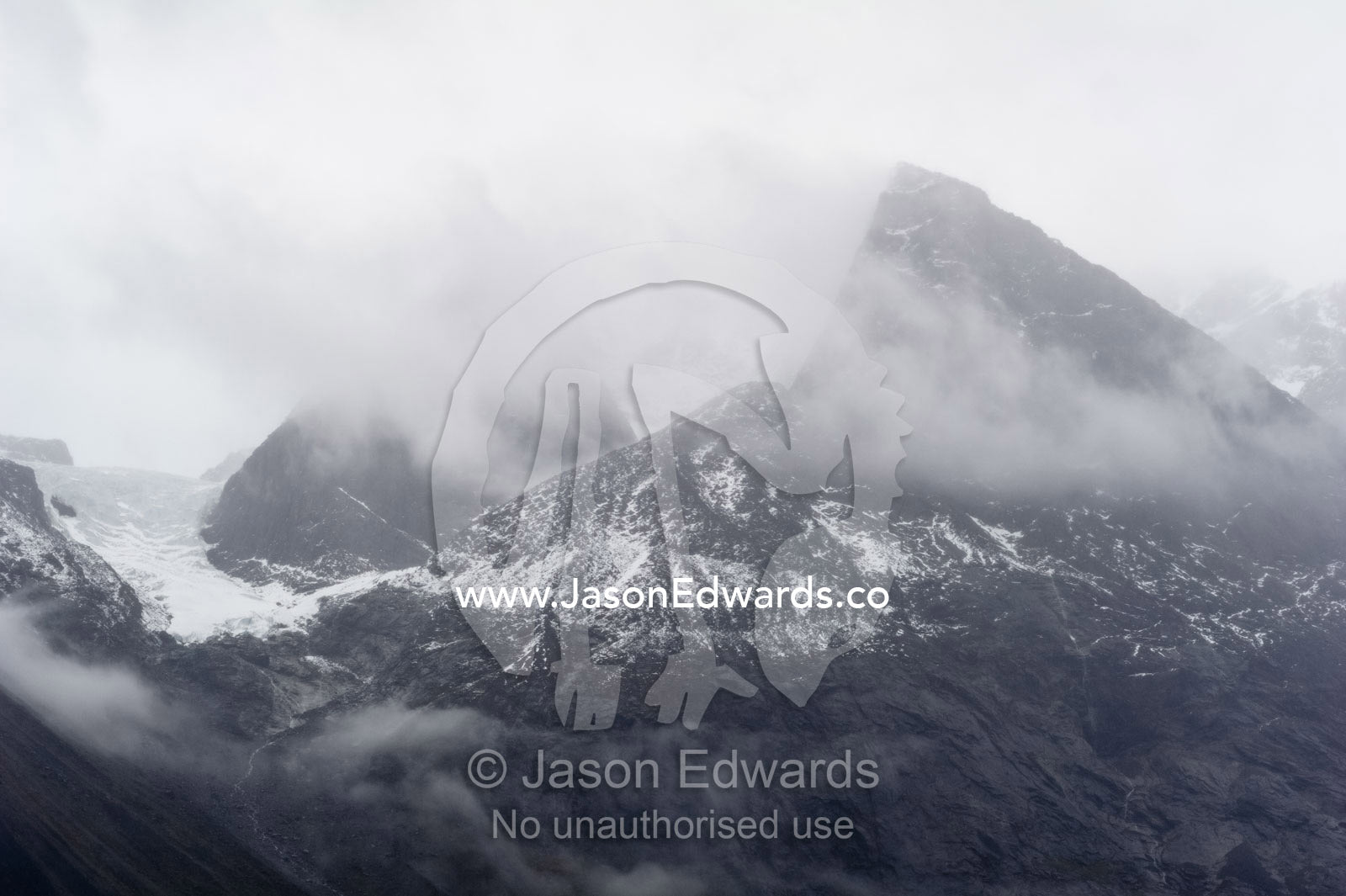 Cloud and mist shroud jagged and rugged mountain peaks during a rain storm in a fiord. Fjord of Eternity, Maniitsoq, Sukkertoppen, Qeqqata Municipality, Greenland.