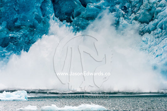 Spray and waves fly into the air after ice carves from a glacier into a fjord. Fjord of Eternity, Maniitsoq, Sukkertoppen, Qeqqata Municipality, Greenland.