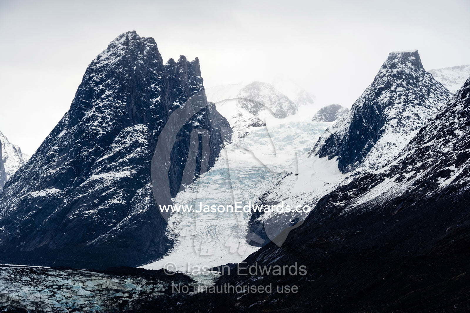 A glacier descends between a pair of mountain peaks in an Arctic fjord. Fjord of Eternity, Maniitsoq, Sukkertoppen, Qeqqata Municipality, Greenland.