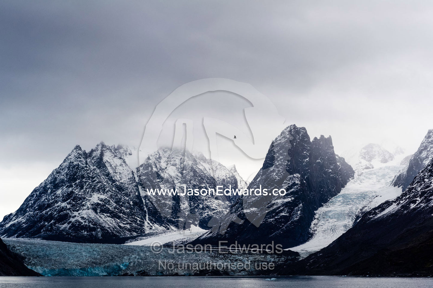 A glacier descends between a pair of mountain peaks in an Arctic fjord. Fjord of Eternity, Maniitsoq, Sukkertoppen, Qeqqata Municipality, Greenland.