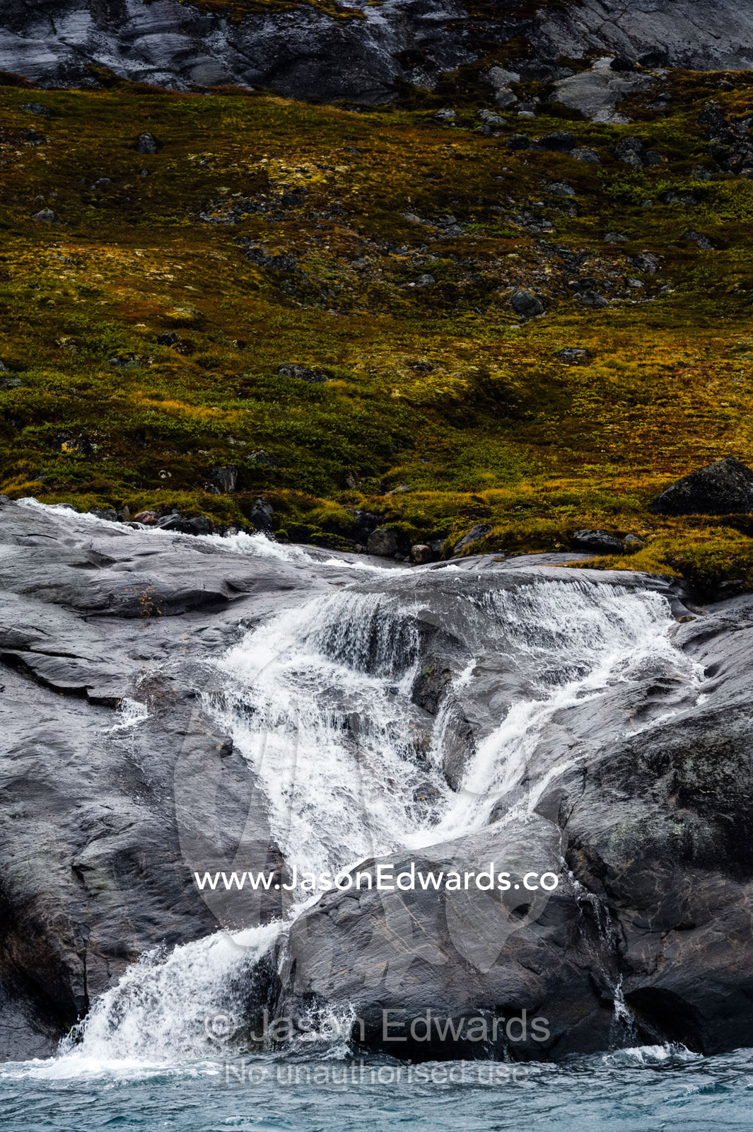 A freshwater stream cascades down a mountainside in an Arctic fjord. Fjord of Eternity, Maniitsoq, Sukkertoppen, Qeqqata Municipality, Greenland.